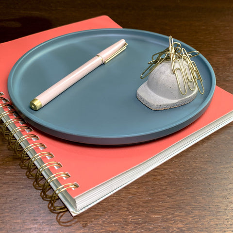 Mini Concrete Hard Hat Magnetic Paperweight Holding Gold Paper Clips Sitting on a Tray Next to a Writing Pen on top of a Journal on a Desk
