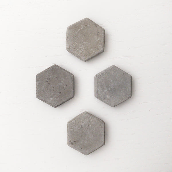 4 hexagon shaped concrete magnets arranged in a honeycomb pattern on a white wood background