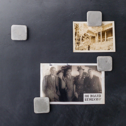 4 square shaped concrete magnets arranged holding black and white photos onto a magnetic chalkboard