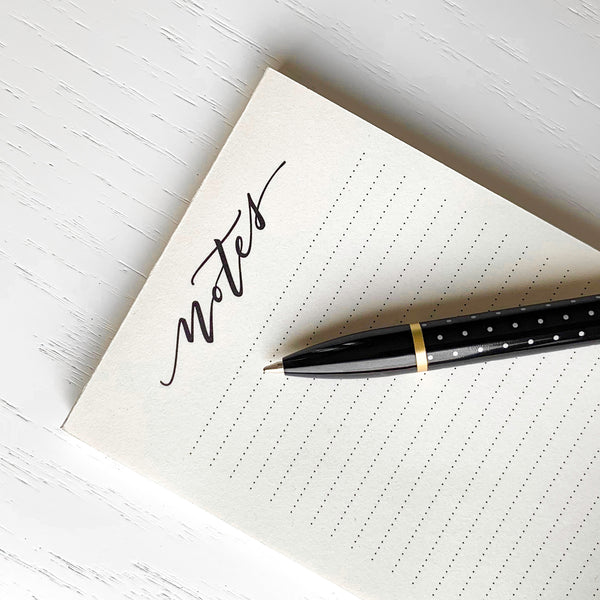 textured paper notepad with dotted lines and handwritten notes header with black and soft gold ubrands ballpoint pen printed with white polka dots